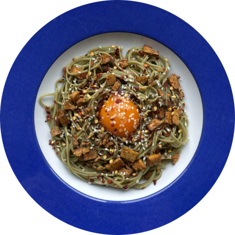Green noodles with cured yolk on blue plate